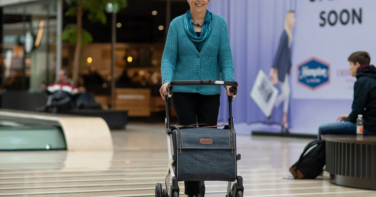 Senior utilisant un rollator 4 roues sur un trottoir, vue de côté, journée ensoleillée