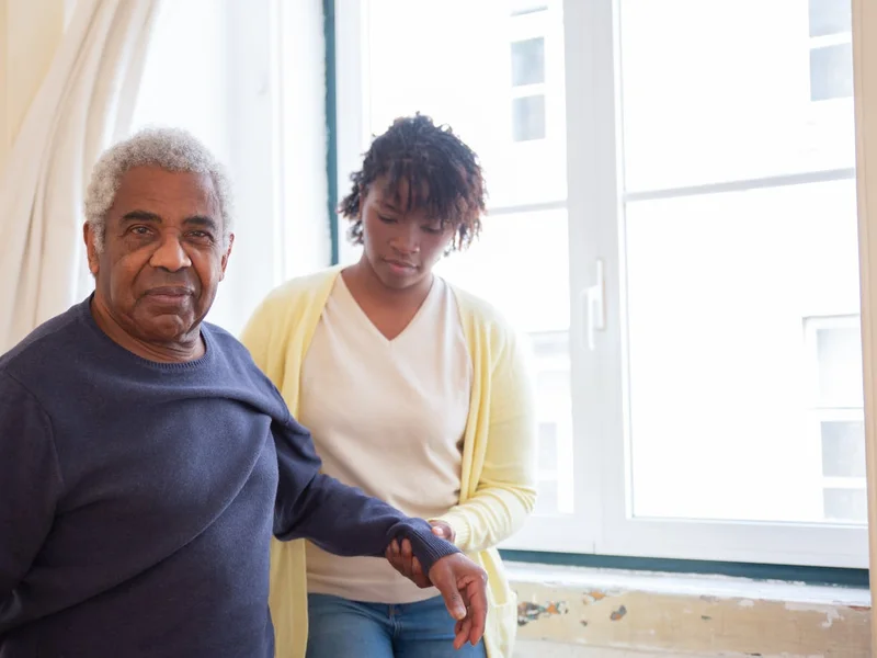 Personne âgée avec son aidant près d&rsquo;une fenêtre — retour à domicile après hospitalisation