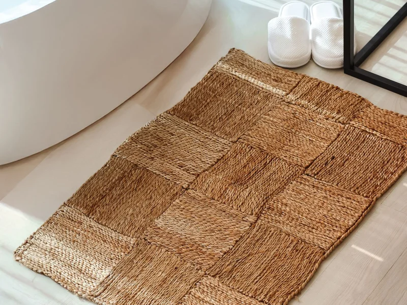 salle de bain lumineuse avec tapis de bain tressé, baignoire et serviettes, ambiance propre et organisée