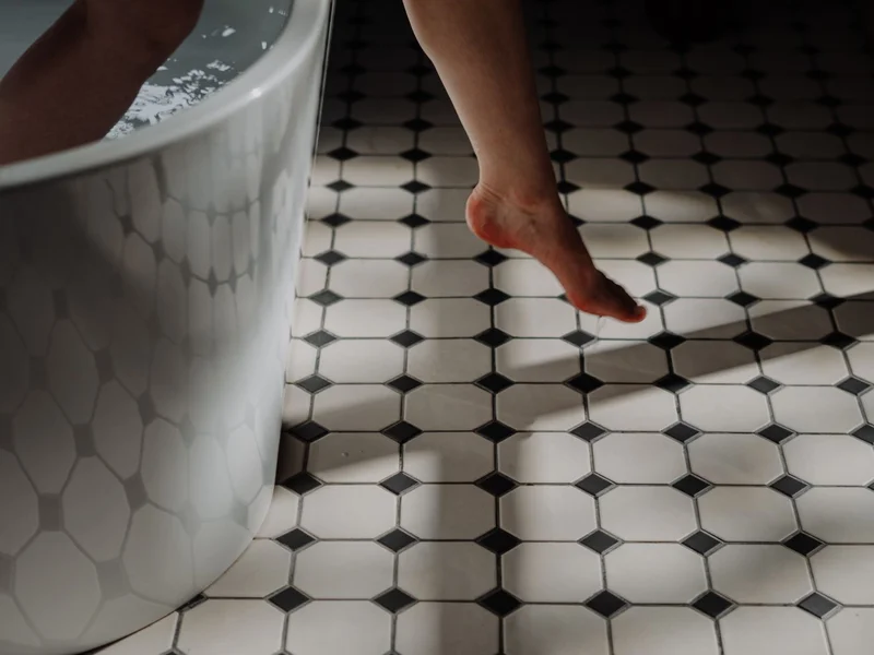 jambe sortant d&rsquo;une baignoire sur carrelage noir et blanc, geste quotidien en salle de bain